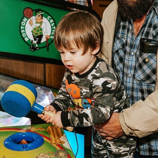 A young boy in camouflage pajamas plays whack-a-mole with an adult's assistance.