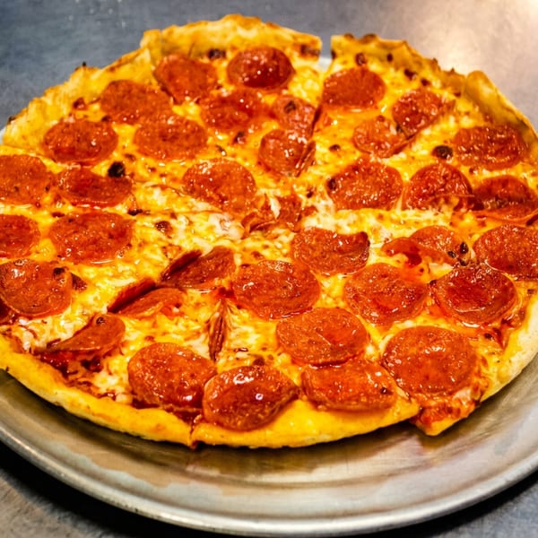 A whole pepperoni pizza with a golden crust sits on a metal pan on a stainless steel surface.