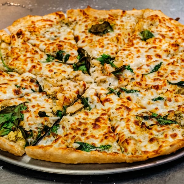 A whole pizza with melted cheese, green spinach, and chicken pieces on a metal tray.