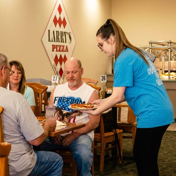 A server delivers a pizza slice to a man at a table in Larry's Pizza restaurant.