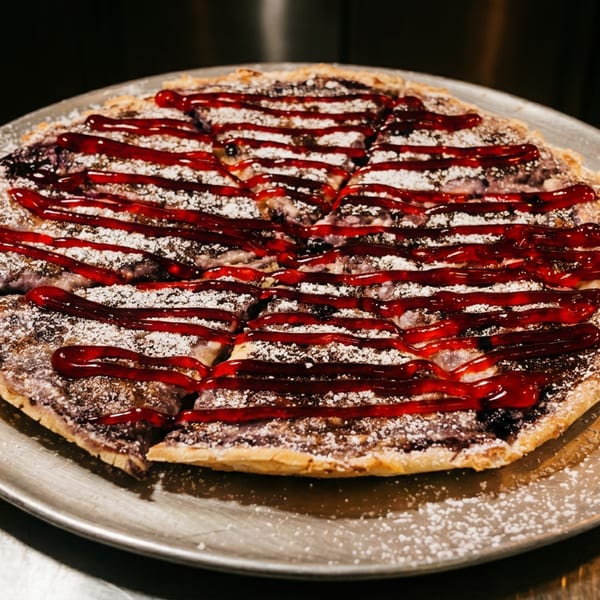 Dessert pizza with blueberry filling, powdered sugar, and raspberry drizzle on a metal tray.