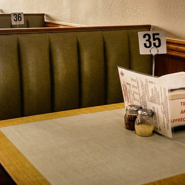 A restaurant booth with a menu, shakers, and a napkin dispenser on a table.