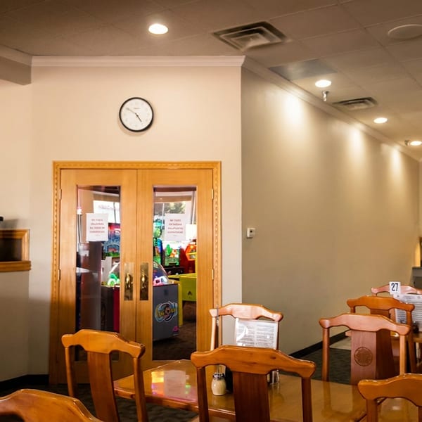 A restaurant dining area with wooden tables and chairs, a buffet line, and an arcade room entrance.