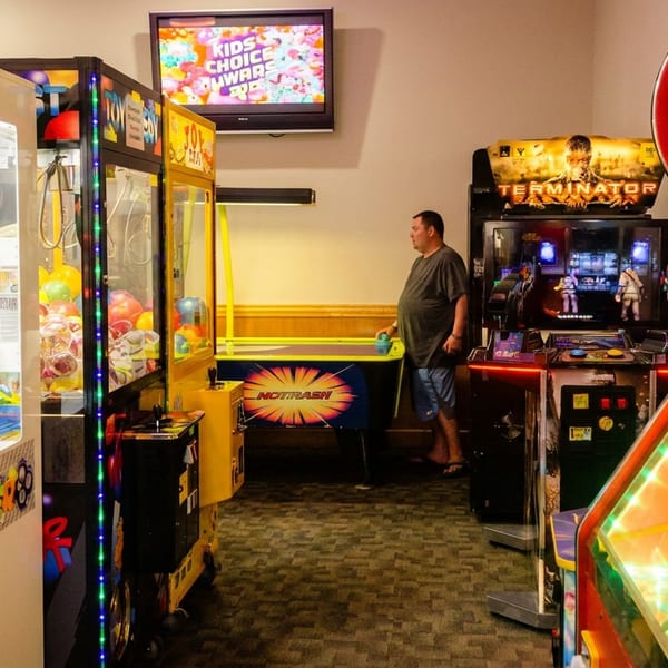 Man playing air hockey in an arcade with claw machines and video games.