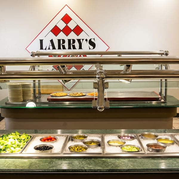 Larry's Pizza buffet with a salad bar in the foreground and pizzas and plates in the background.