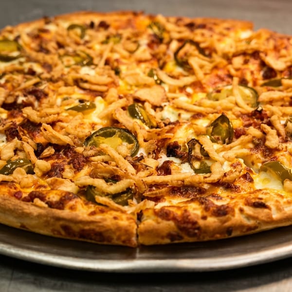 A whole pizza with jalapeños and crispy fried onions on a metal pan.